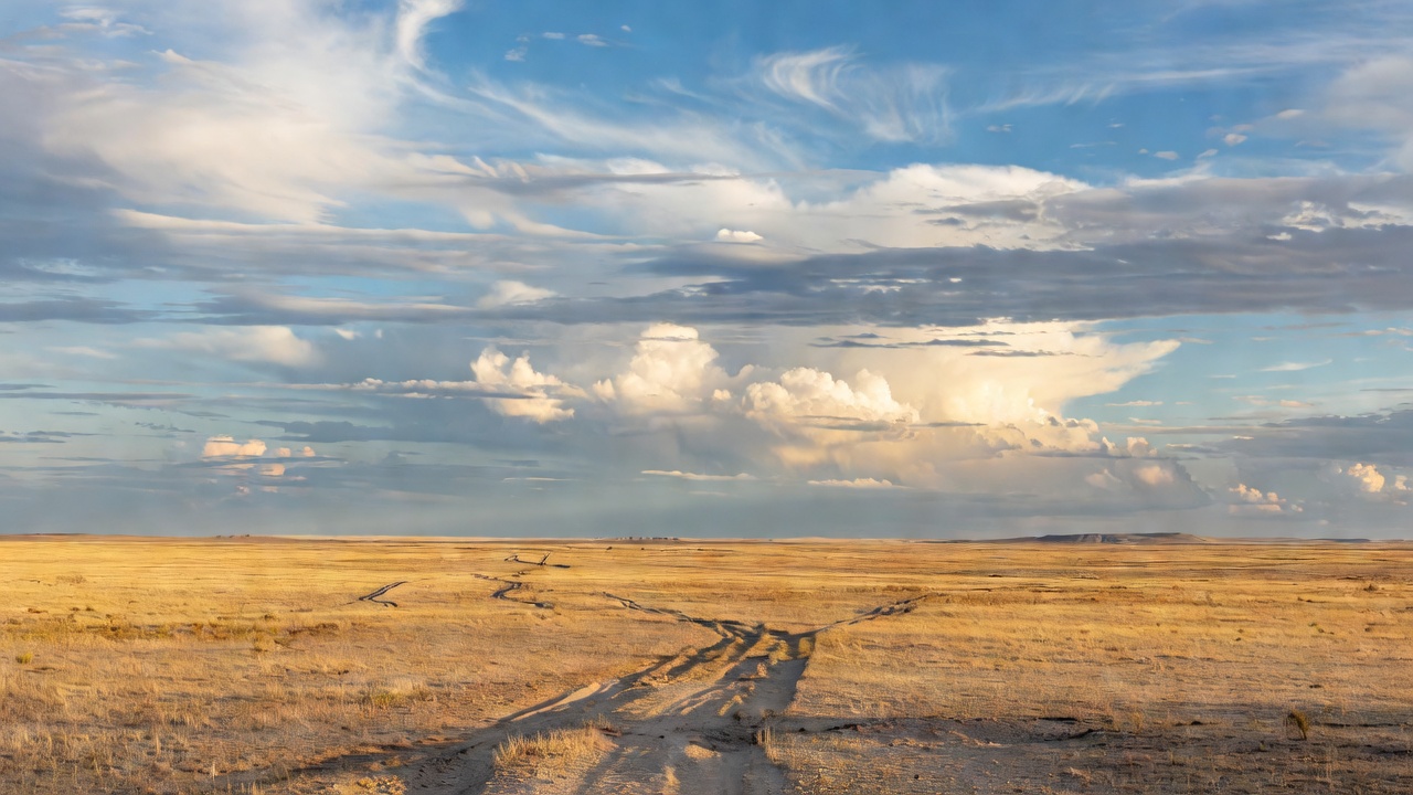Expansive open plain with a subtle track and a wide sky filled with layered cloud